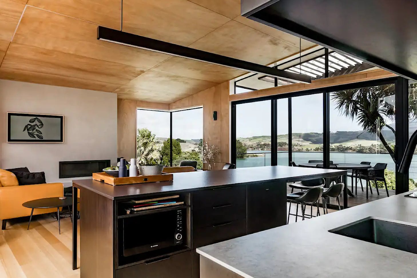 A modern kitchen looks out onto a spacious dining room and view of Mt Karioi at this Raglan airbnb.